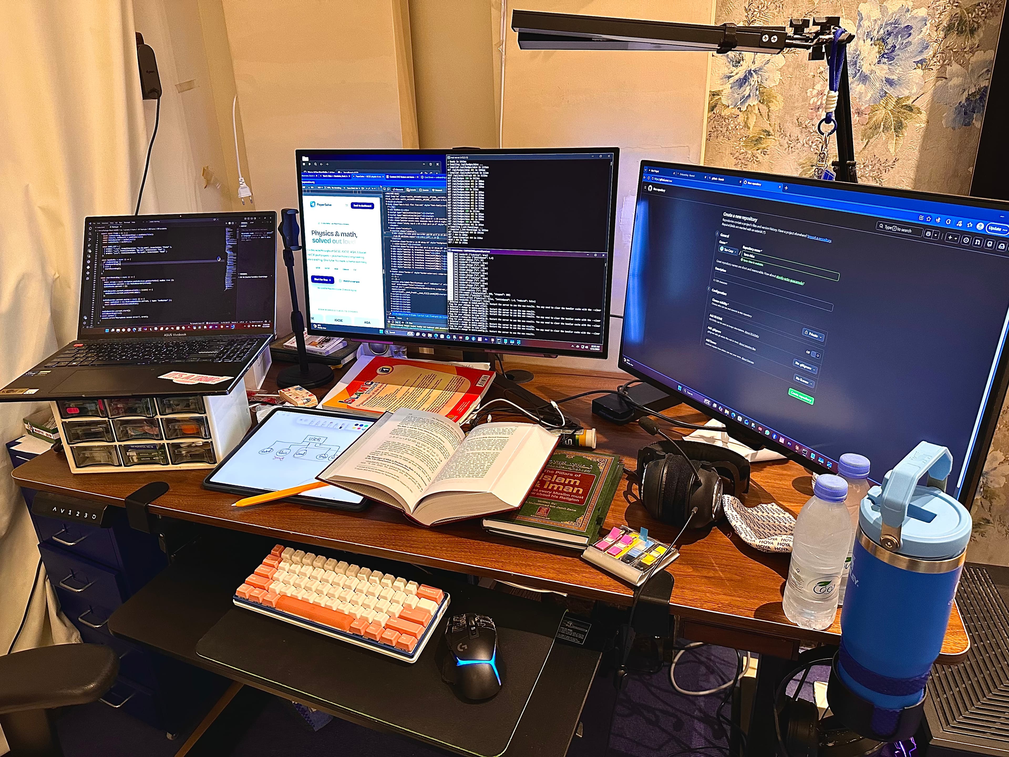 Yarra's workspace in Riyadh — three screens of code, an open Quran and an architecture notebook, her Islamic Studies book, and a mechanical keyboard